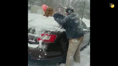 Il papà usa il bimbo per togliere la neve dalla macchina